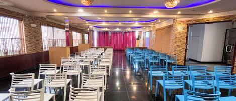 A conference room with rows of white and blue chairs, a stage with a red curtain, and a chandelier.