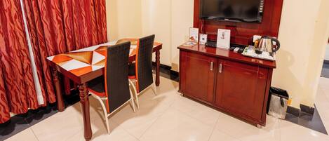 A dining area with a table and chairs, a TV mounted on a wooden cabinet, and a trash bin.