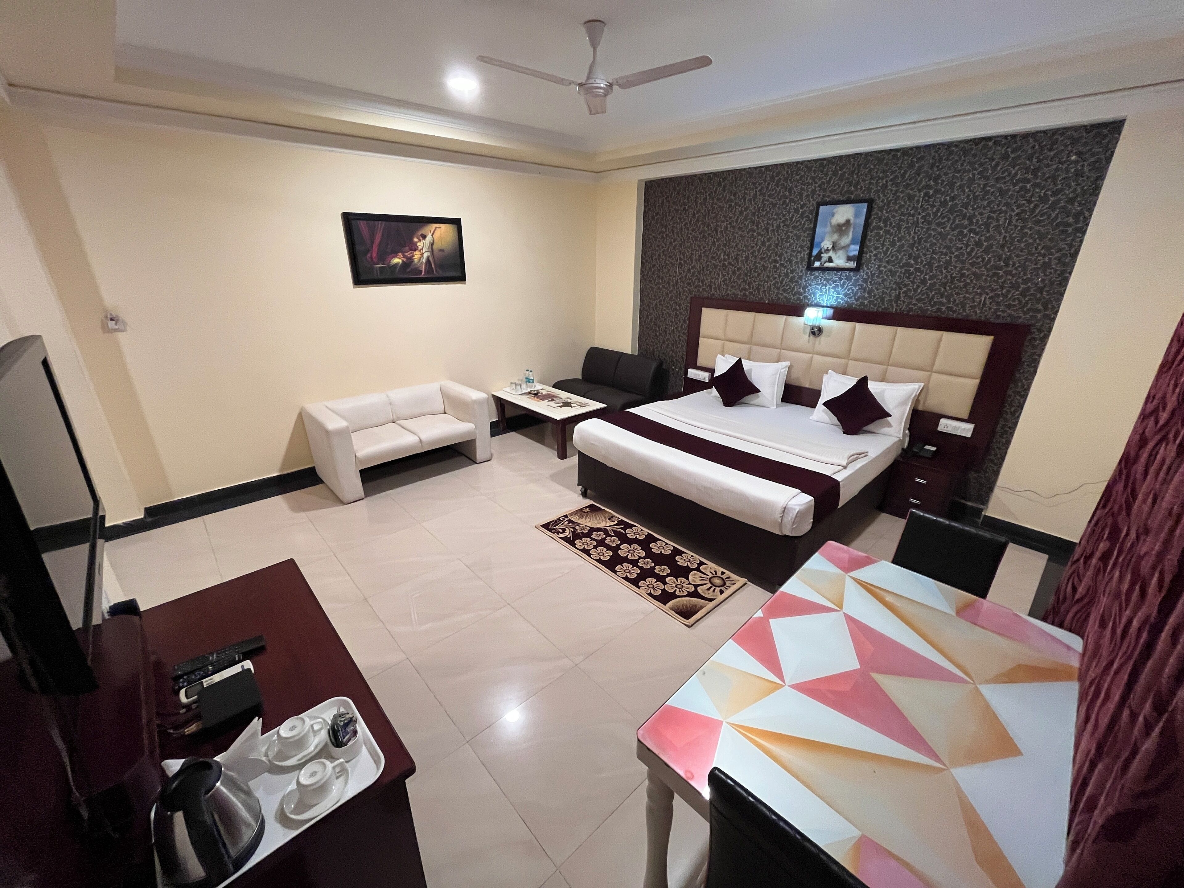 A hotel room with a bed, a sofa, a desk with a tray of tea, and a ceiling fan.