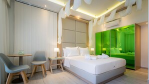 A modern hotel room with a large bed, a desk with two chairs, a small table, and a green accent wall. - Lobelia Luxury Suites (Thasos)