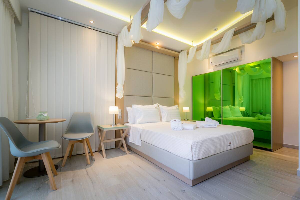Una habitación de hotel moderna con una cama grande, un escritorio con dos sillas, una mesita y una pared de acento verde.