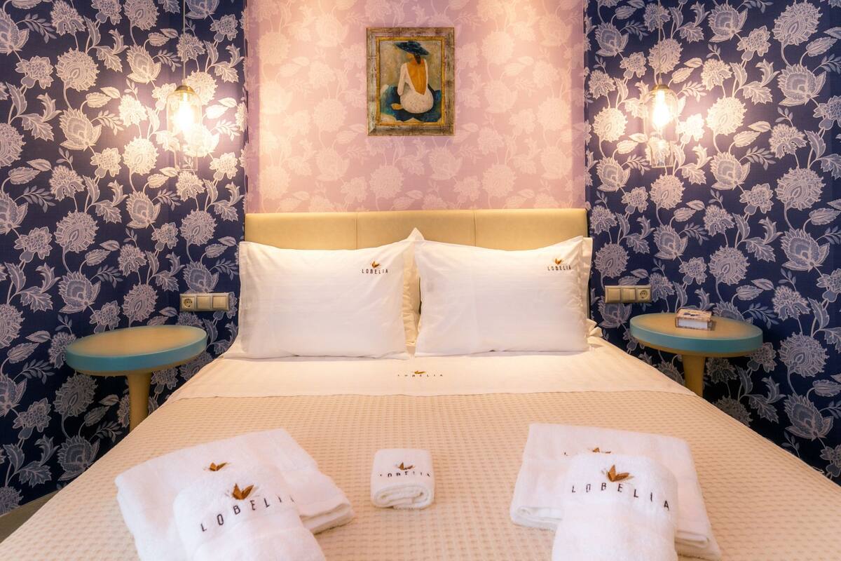 Habitación de hotel con cama, dos mesitas de noche, un cuadro en la pared y toallas con el nombre del hotel.