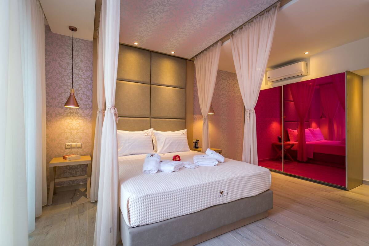 Una habitación de hotel moderna con una cama grande, una mesita de noche, un equipo de aire acondicionado y una habitación iluminada en rojo a la derecha.