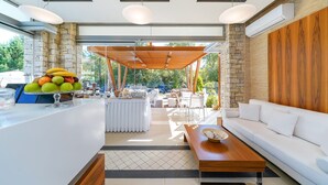 A modern outdoor dining area with a stone wall, wooden pergola, and a white sofa. - Lobelia Luxury Suites (Thasos)