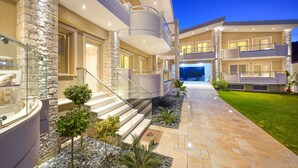 A modern multi-story house with a stone facade, a glass-enclosed bathroom, and a well-lit outdoor area with a paved walkway and small plants. - Lobelia Luxury Suites (Thasos)