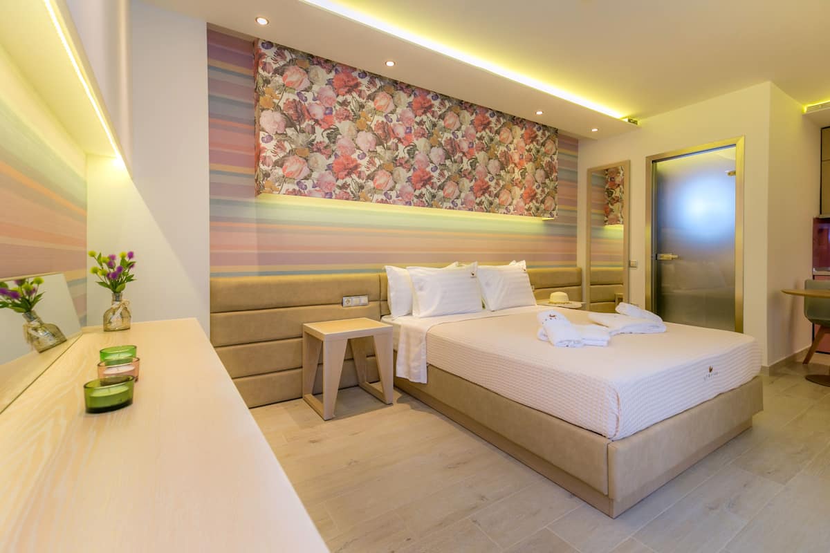 Una habitación de hotel moderna con una cama grande, mesitas de noche, un tocador con espejo y un papel tapiz estampado con motivos florales.