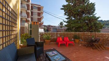 A rooftop terrace with wicker furniture, potted plants, and a view of the cityscape.