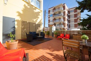 An outdoor patio area with a seating arrangement, potted plants, and a view of a multi-story building.