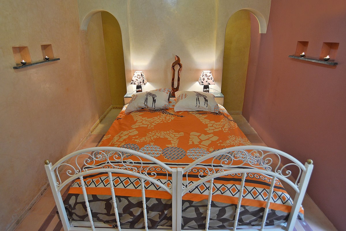 A narrow room with a bed, two bedside tables with lamps, and a decorative wall piece.