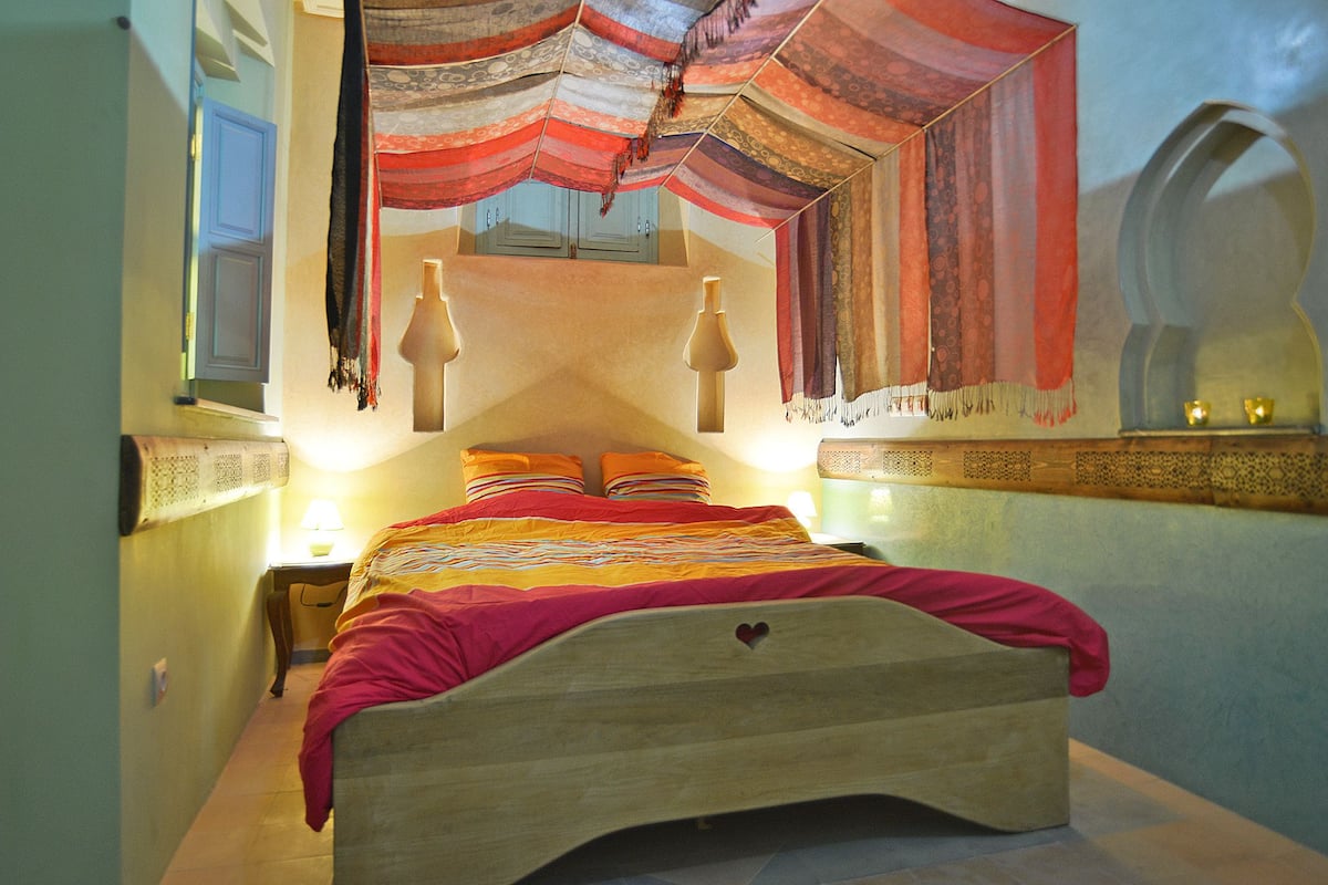 A bedroom with a wooden bed, a nightstand, a lamp, and a decorative wall hanging.