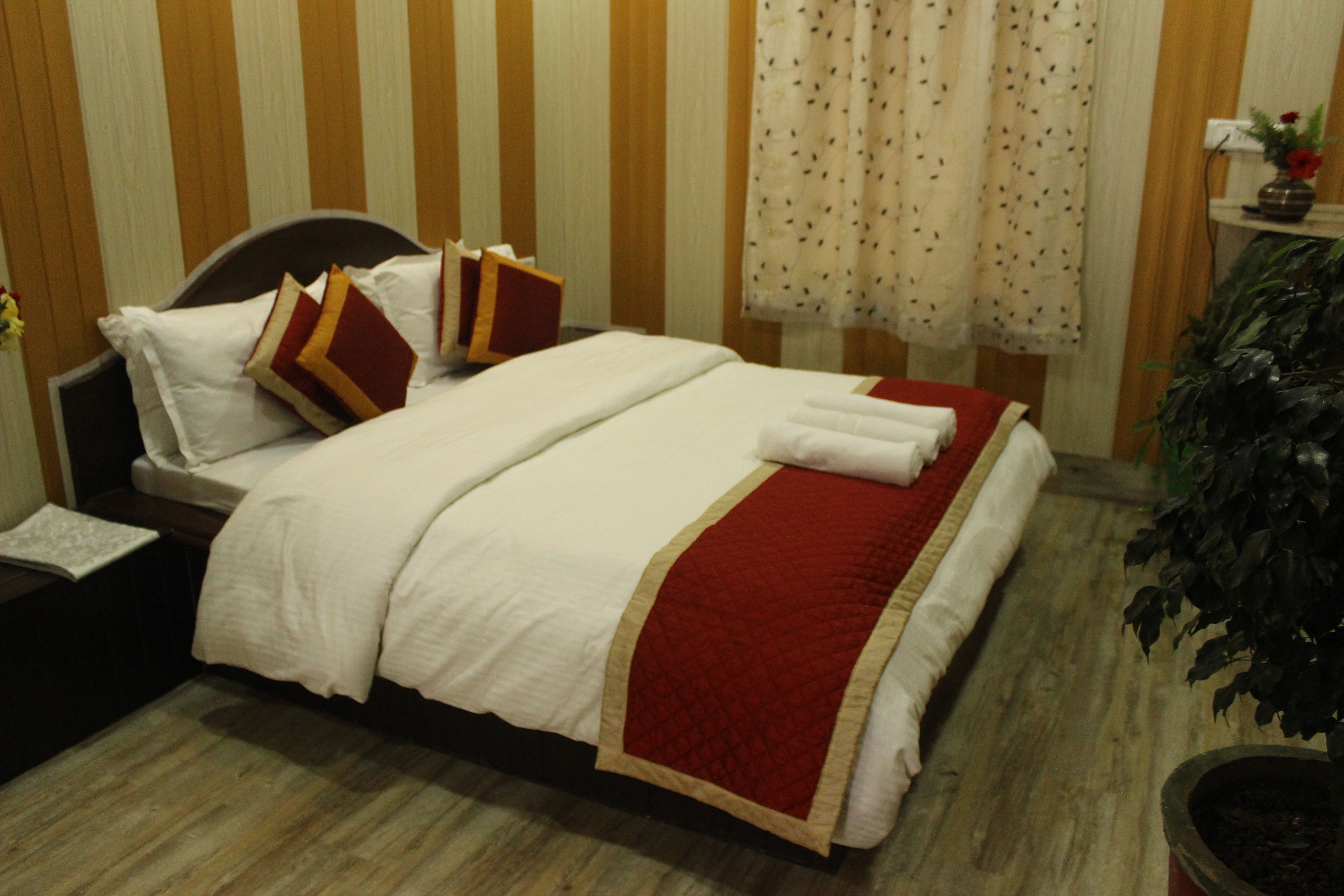 Una cama bien hecha con ropa de cama blanca y roja, un cabecero oscuro y un piso de madera.