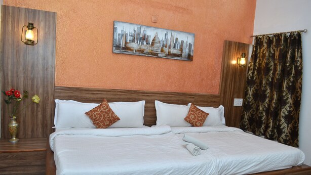 A hotel room with a large bed, wooden headboard, a cityscape painting, and a vase with flowers. - Hotel Shanti Mount Abu (Abu Road)