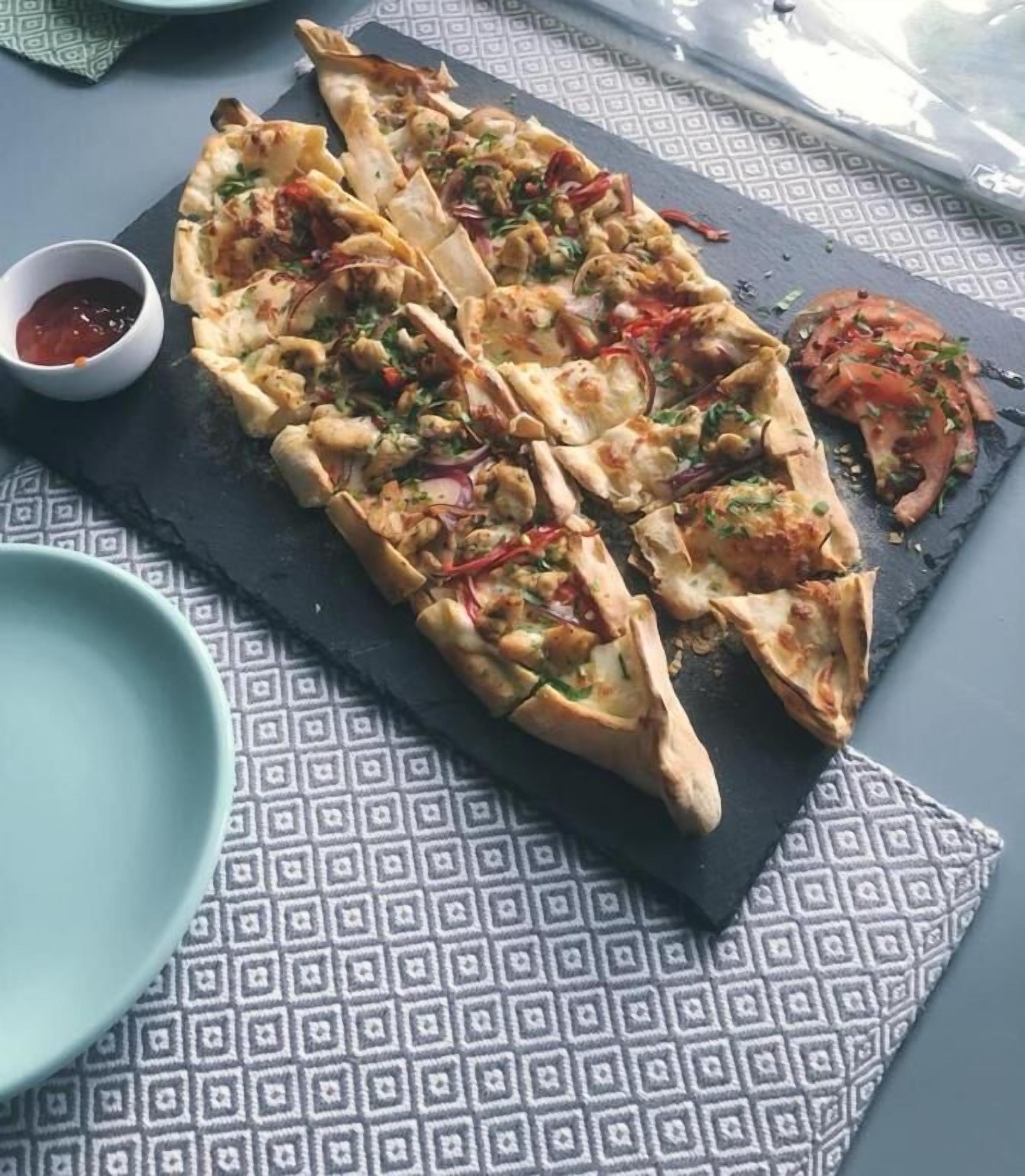 A flatbread dish with toppings, a small bowl of sauce, and a patterned napkin on a table.