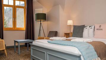 Una habitación de hotel con cama, mesita de noche, lámpara, silla y ventana con cortinas.