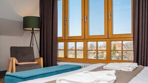 A hotel room with a bed, a chair, a massage table, and a large window with curtains. - Conacul Törzburg (Bran)