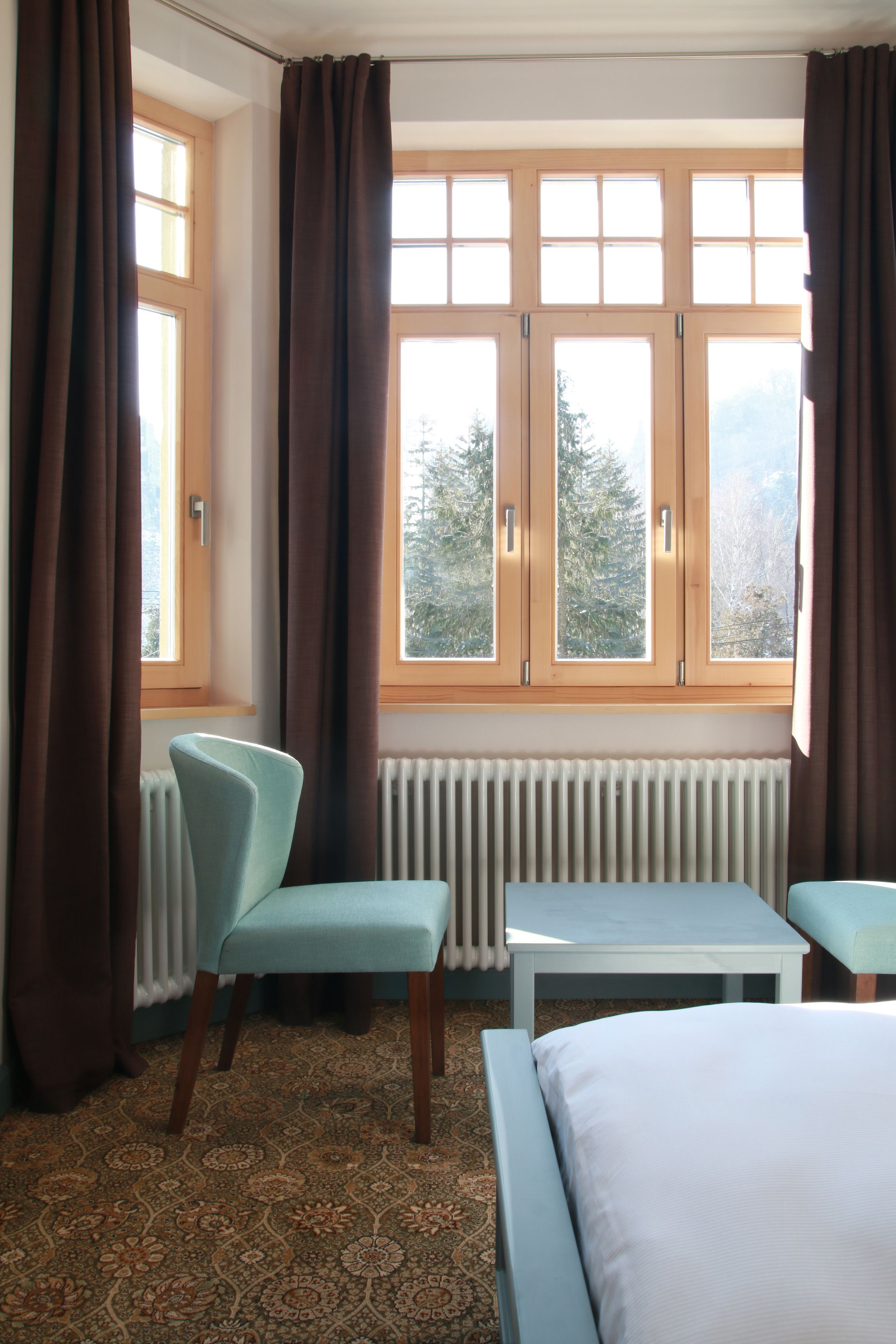 Ein Hotelzimmer mit einem Bett, einem Sessel, einem Tisch und einem Vorhangfenster.