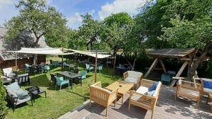 Un patio al aire libre con mesas y sillas, rodeado de árboles y una terraza de madera.