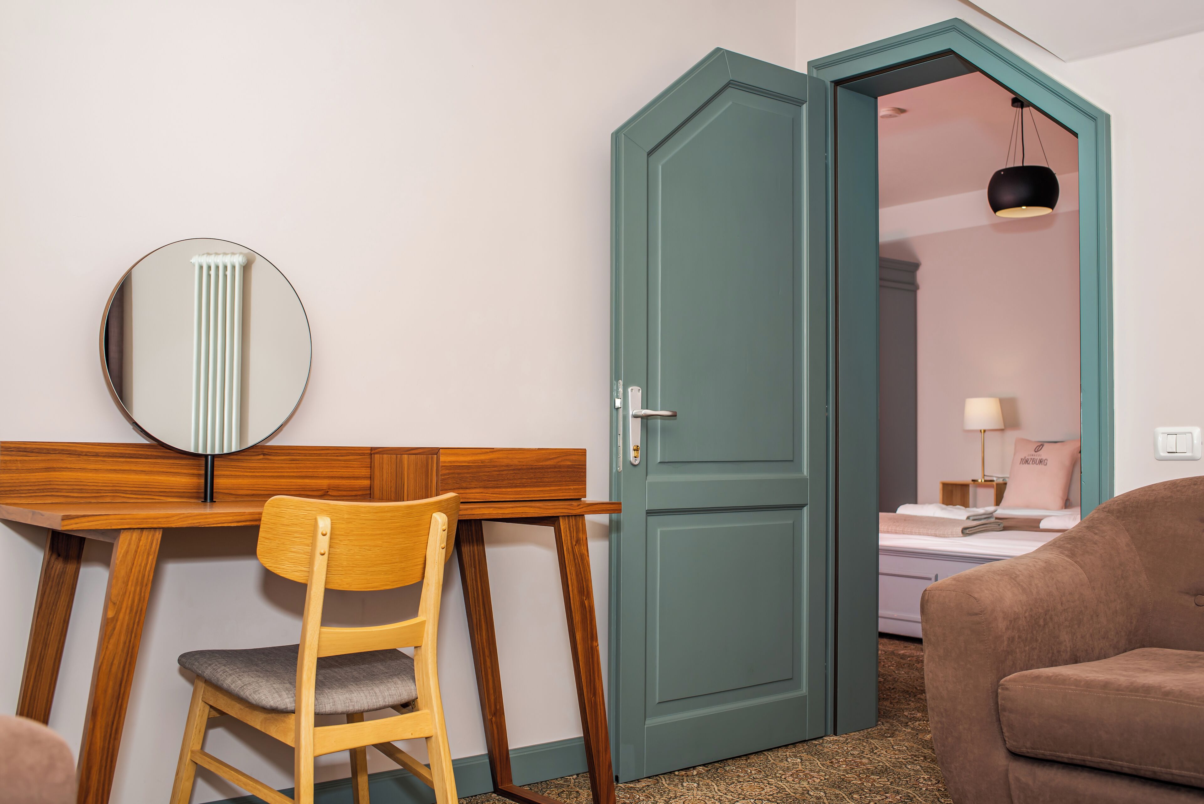 A room with a wooden desk, a chair, a bed with a pillow, and a green door.
