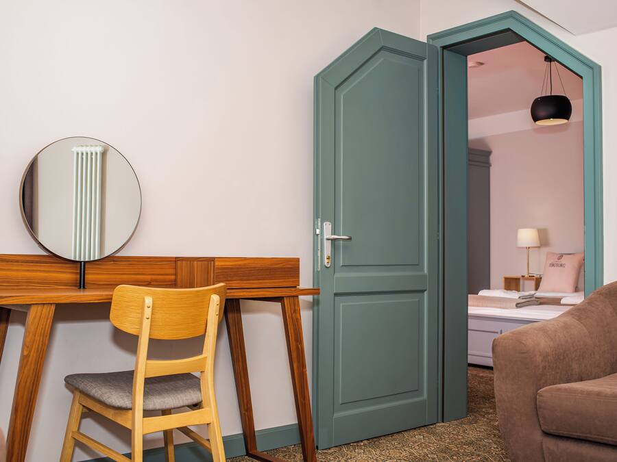 Una habitación con un escritorio de madera, una silla, una cama con un almohadón y una puerta verde.