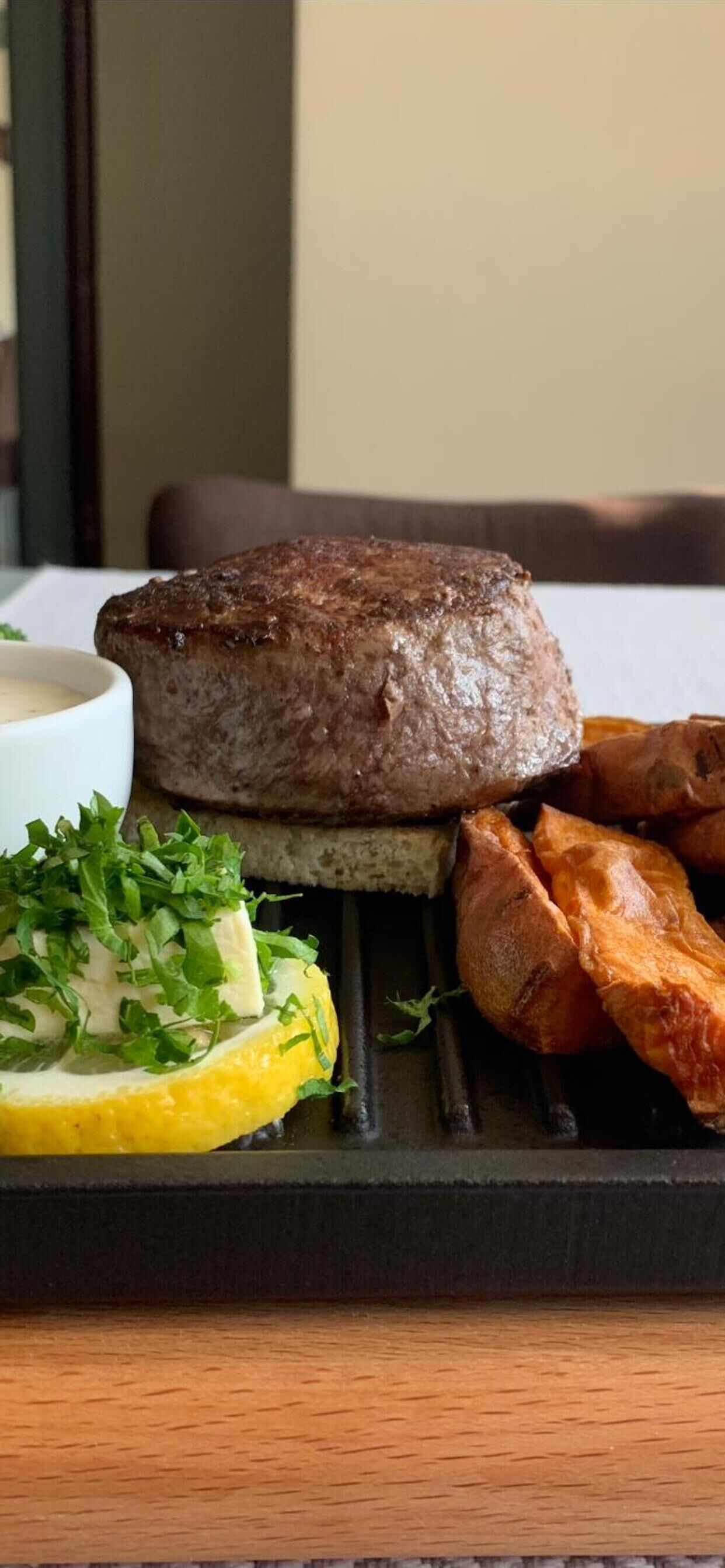A steak on a grill with a side of roasted potatoes and a slice of lemon.