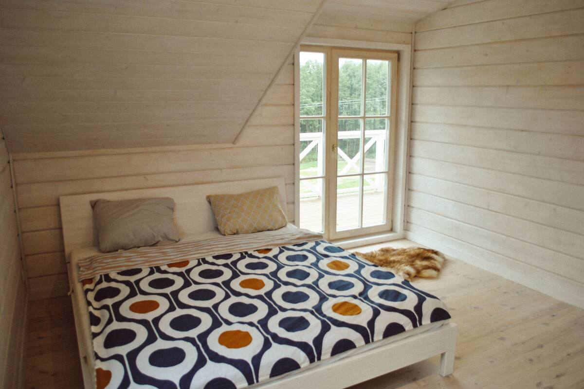 Ett sovrum med en säng, kuddar, ett fönster och utsikt över en träveranda.