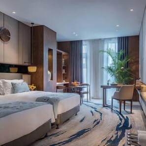 A modern hotel room with a large bed, a desk, and a chair. There is a plant and a window with curtains. - Yannian Plaza Hotel (Zhuzhou)