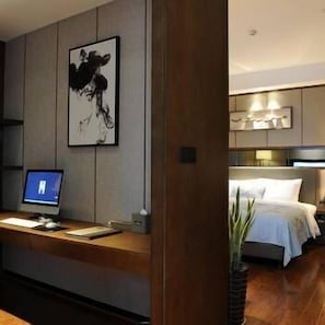 A modern hotel room with a wooden desk, a computer, a bed with white linens, and a large abstract painting on the wall. - Yannian Plaza Hotel (Zhuzhou)