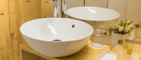 Une salle de bain avec deux lavabos blancs, une douche en verre, des murs en bois et un meuble-lavabo en bois sur lequel se trouve un plateau contenant des articles de toilette.