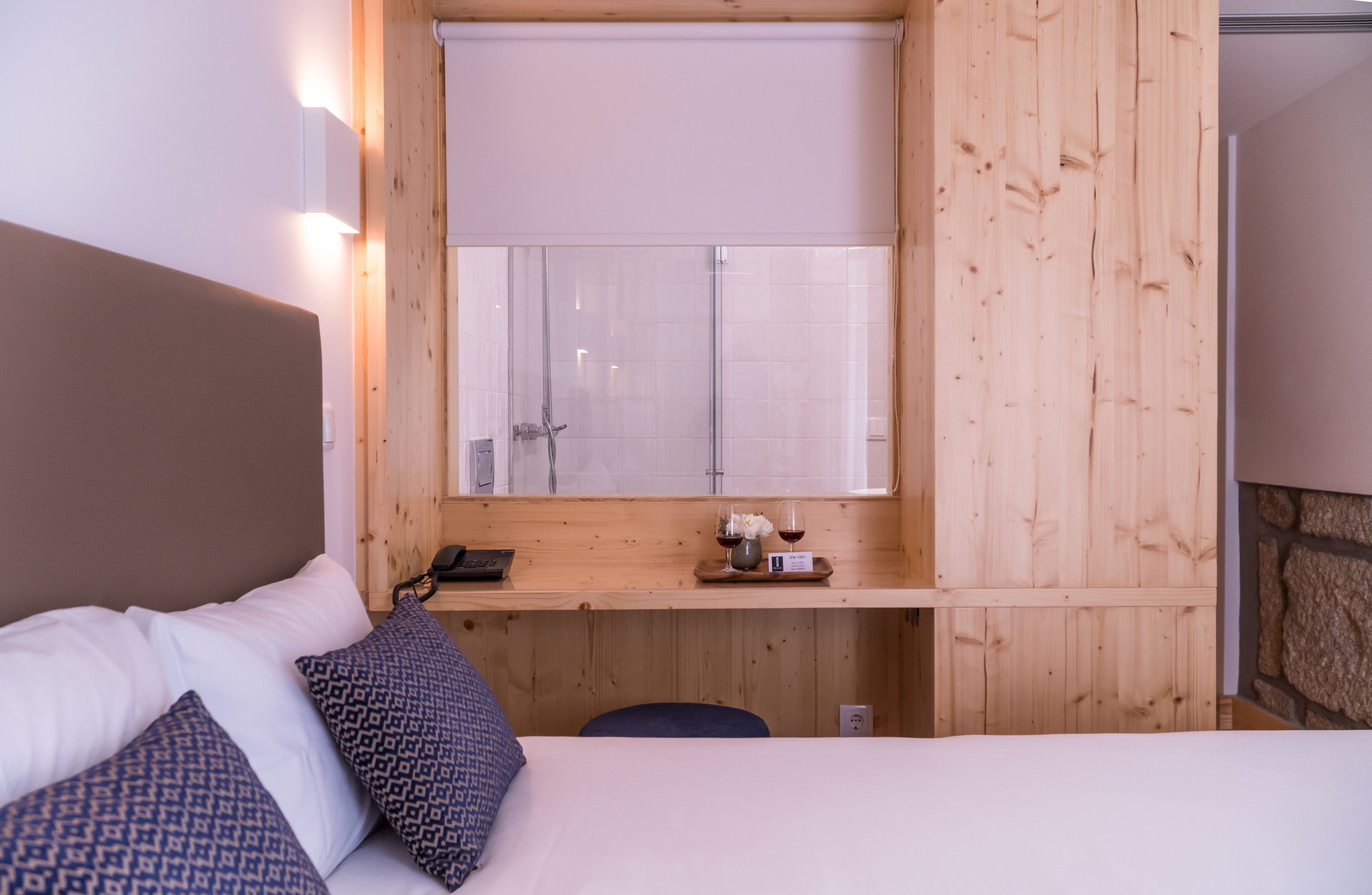 A wooden-paneled room with a bed, a small table with a phone and glasses, and a window with a view.
