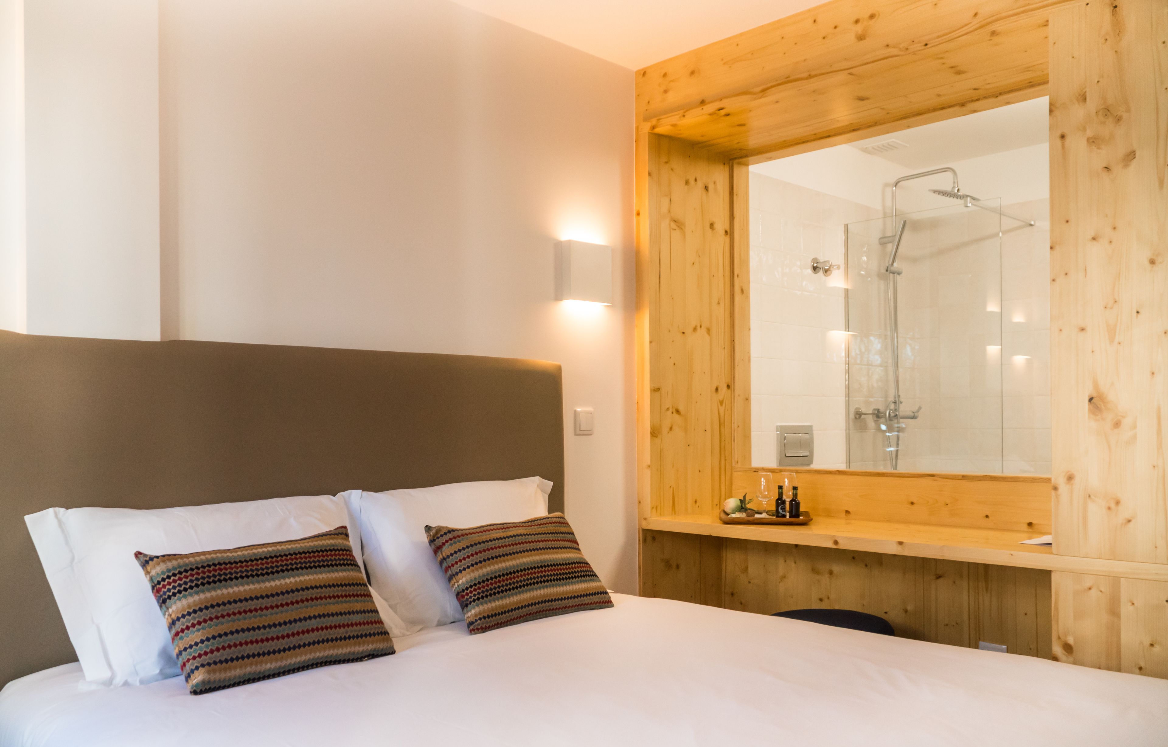 A hotel room with a wooden headboard, a large mirror, and a shower area visible through the glass.