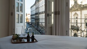 Habitació d'hotel amb un llit, una bandeja amb copes i ampolles de vi, i una vista d'edificis a través d'una finestra.