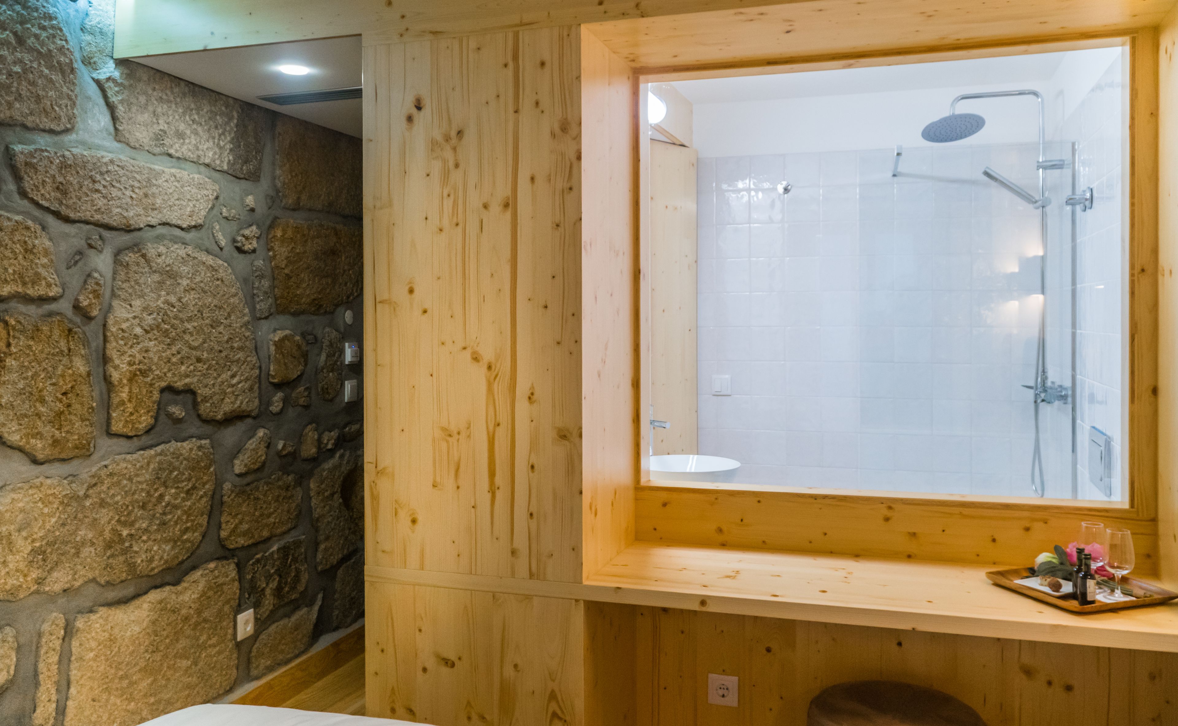Een badkamer met een stenen muur, houten lambrisering, een grote spiegel en een douche.
