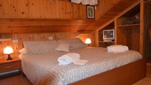 A wooden-paneled bedroom with a bed, two bedside tables with lamps, and a television on a shelf. - Campodolcino Camping (Campodolcino)