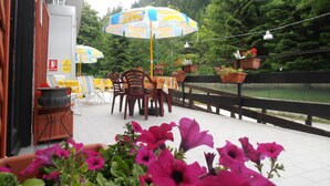 An outdoor patio with tables and chairs, umbrellas, and potted plants. - Campodolcino Camping (Campodolcino)