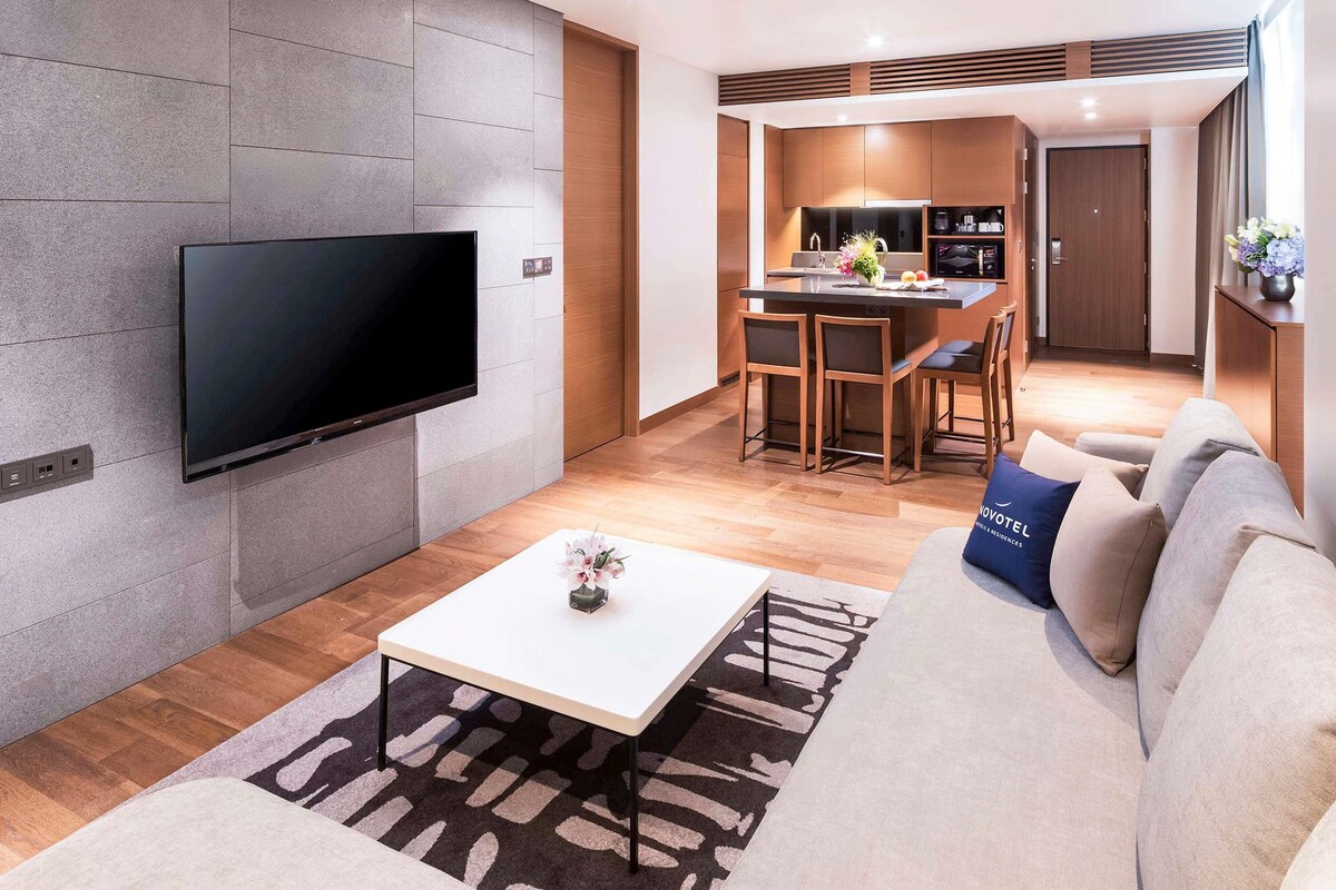 A modern living room with a flat-screen TV mounted on a textured wall, a sofa with a decorative pillow, and a coffee table with a vase.