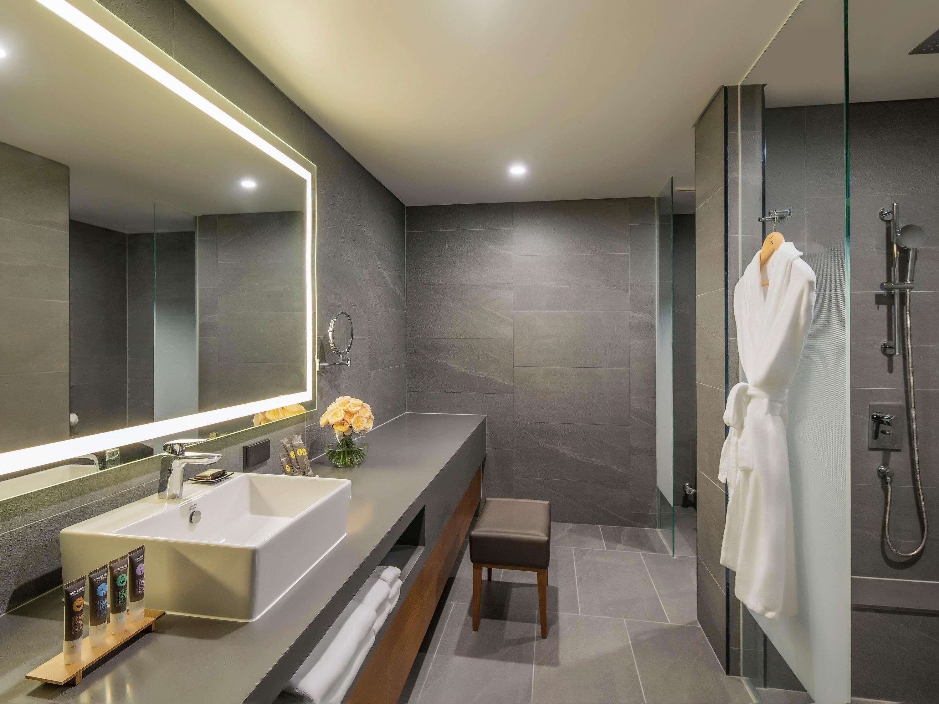 Un baño moderno con un espejo grande, un lavamanos, una ducha y una bata colgada en la pared.