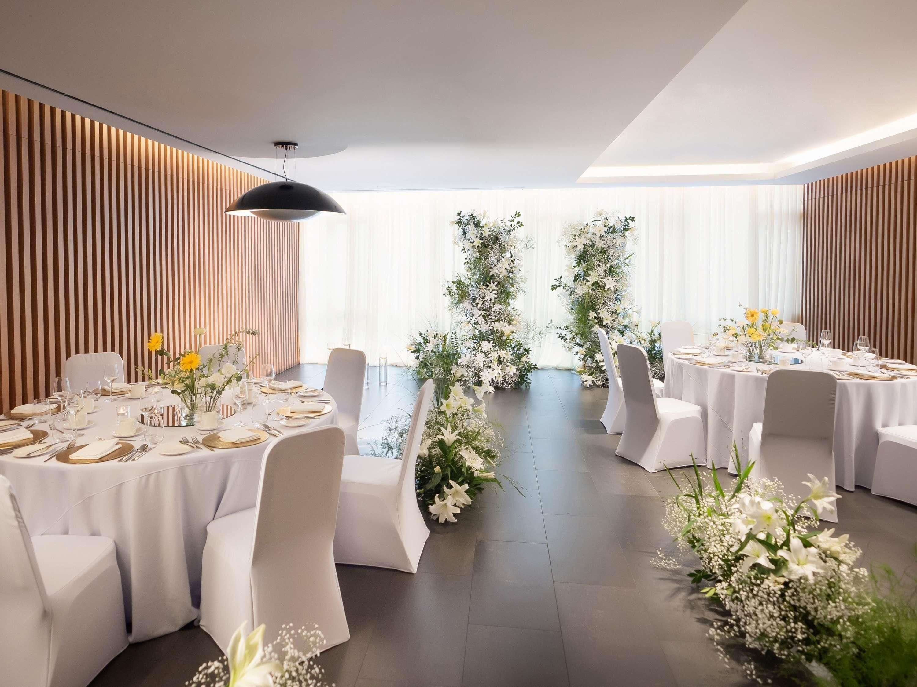 A modern dining area with round tables, white chairs, and floral centerpieces.