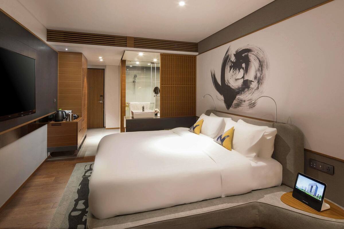 Une chambre d’hôtel moderne dotée d’un grand lit, d’une télévision, d’une salle de bain avec douche et d’une œuvre d’art murale.