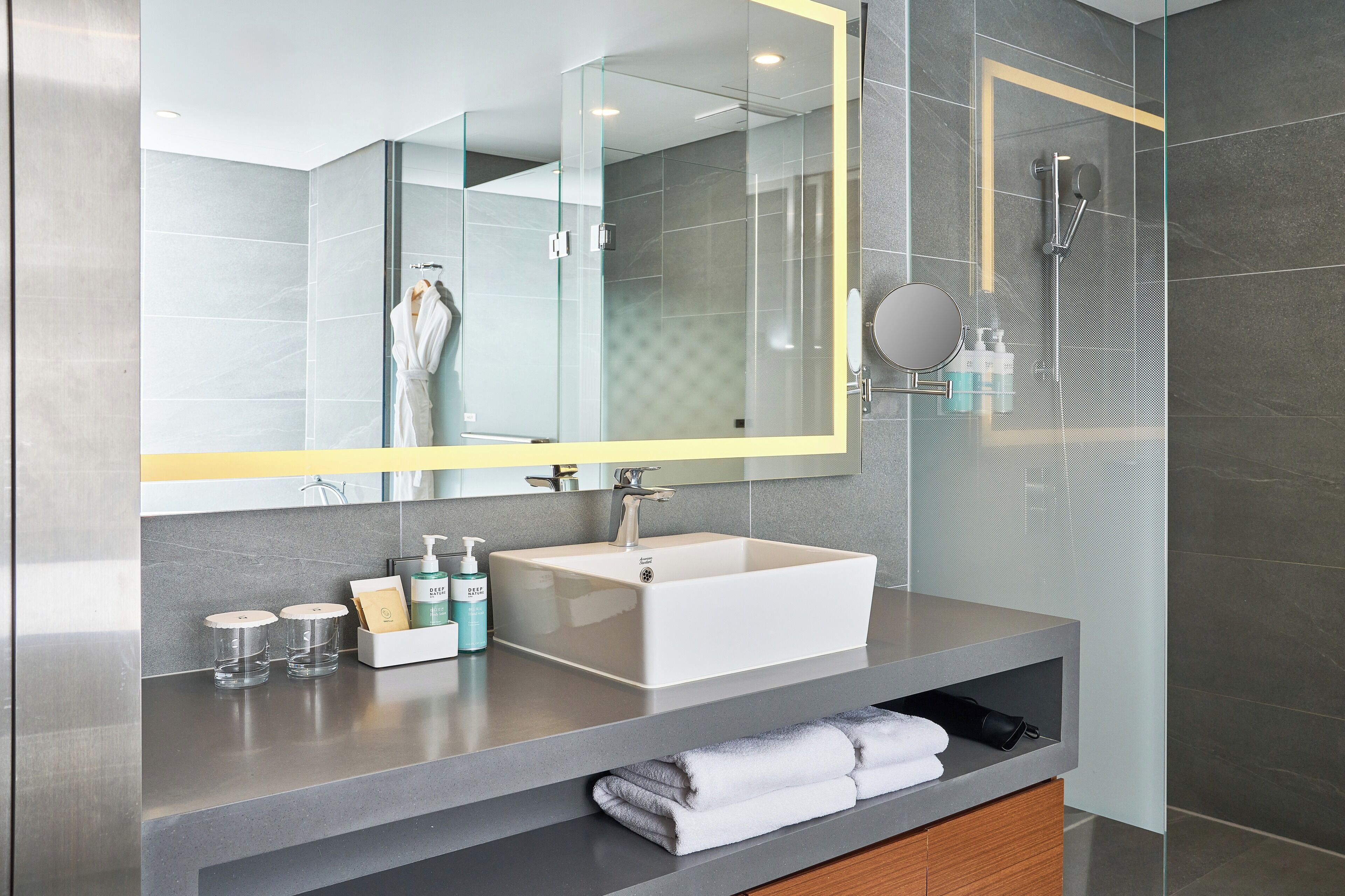 Een moderne badkamer met een grote spiegel, een witte wastafel en een douche met glazen wanden.