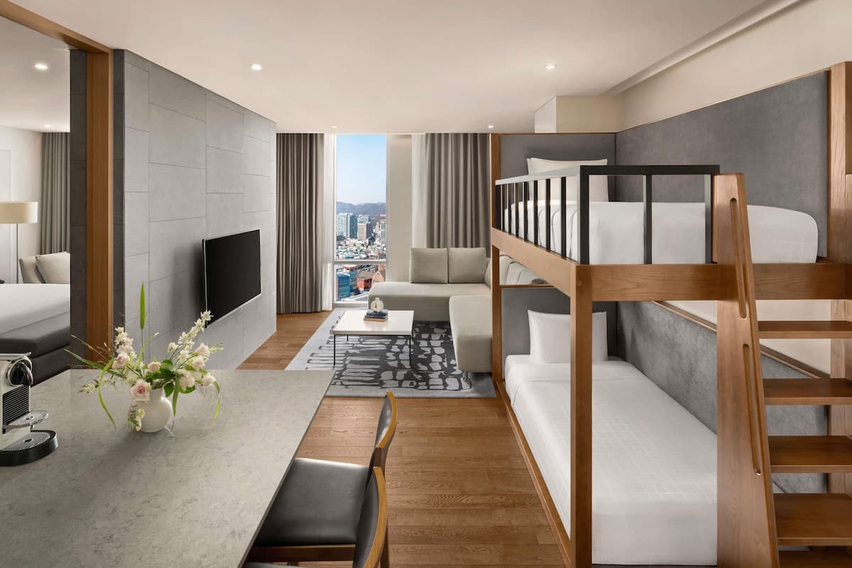 Une chambre d’hôtel moderne équipée d’un lit superposé, d’un téléviseur à écran plat, d’un coin repas avec une machine à café et offrant une vue sur la ville.