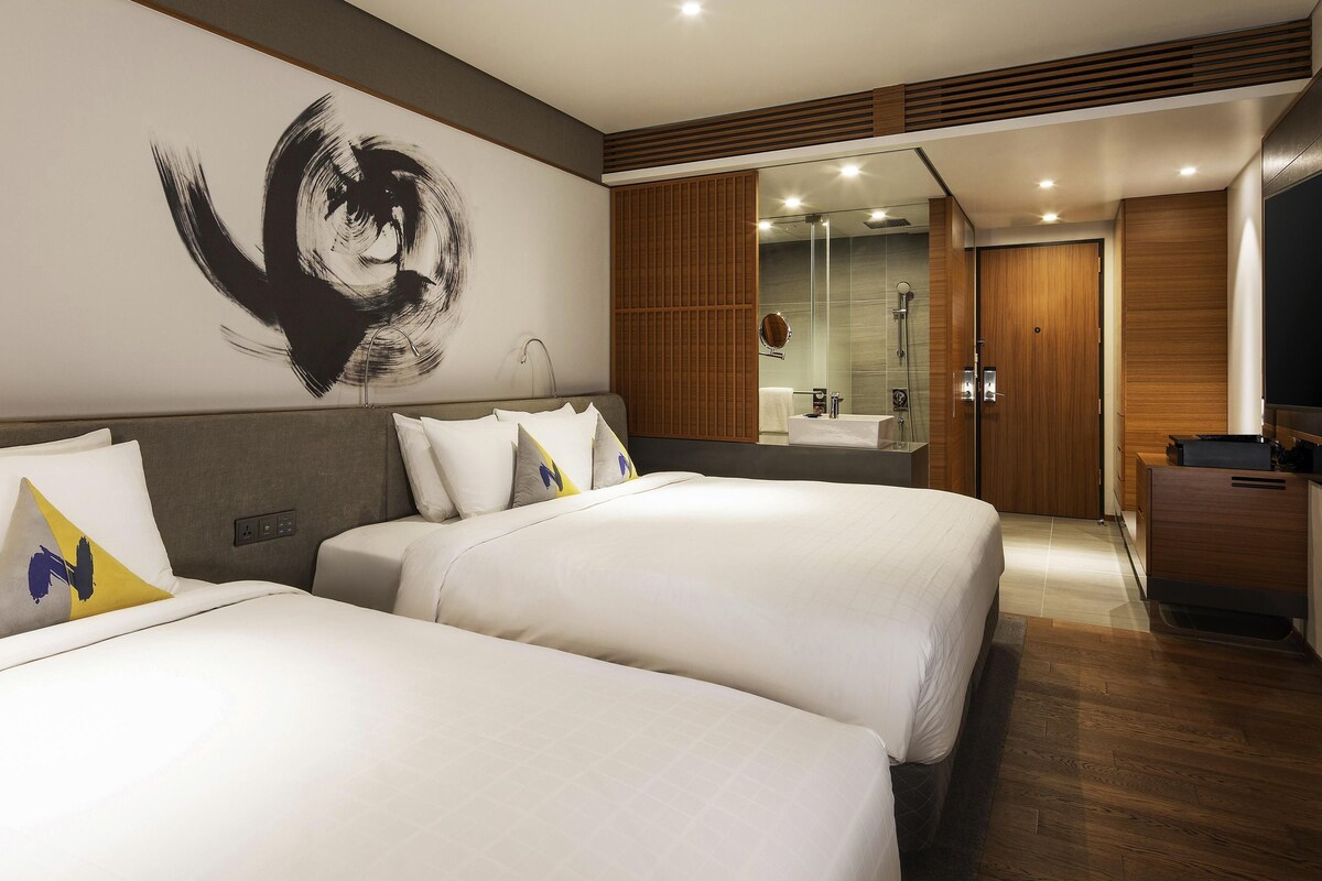 A hotel room with two beds, a large abstract painting, a modern bathroom, and wooden paneling.