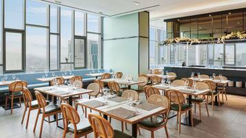 A restaurant with high tables and chairs, large windows, and a city view.