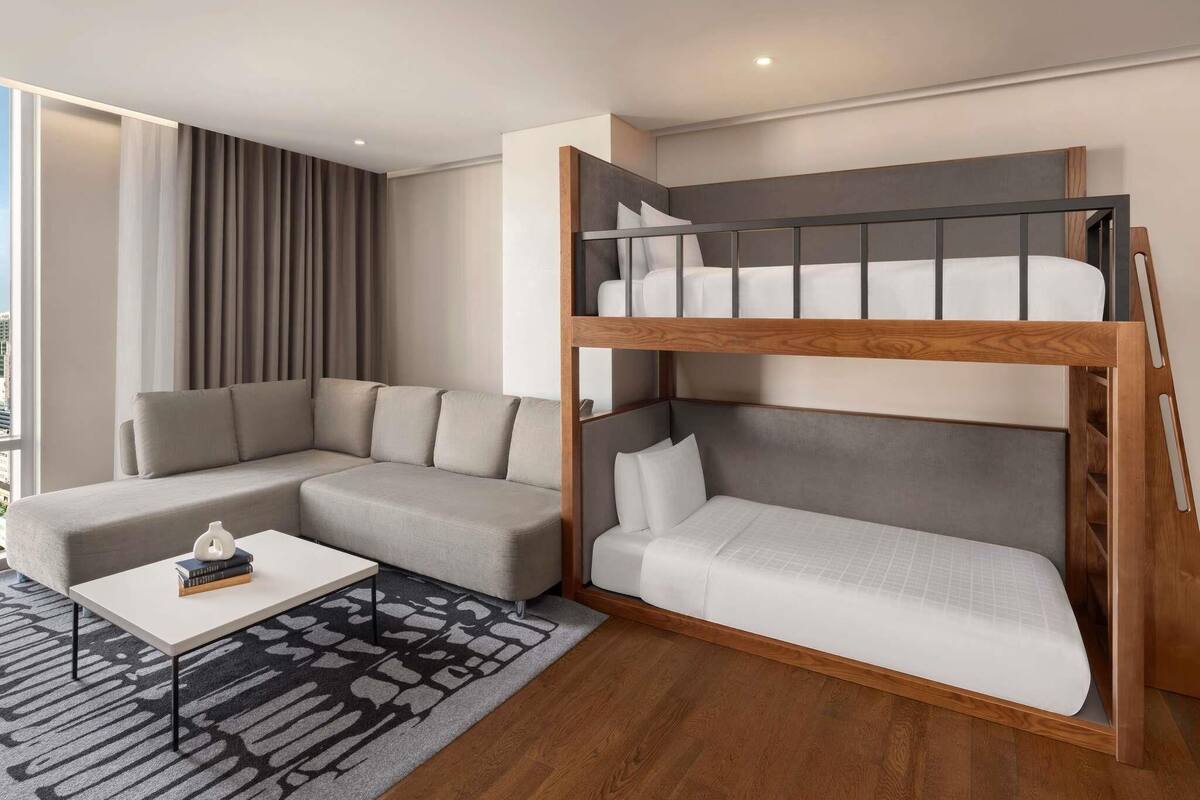 Una habitación moderna con una litera, un sofá, una mesa de centro y una alfombra estampada.