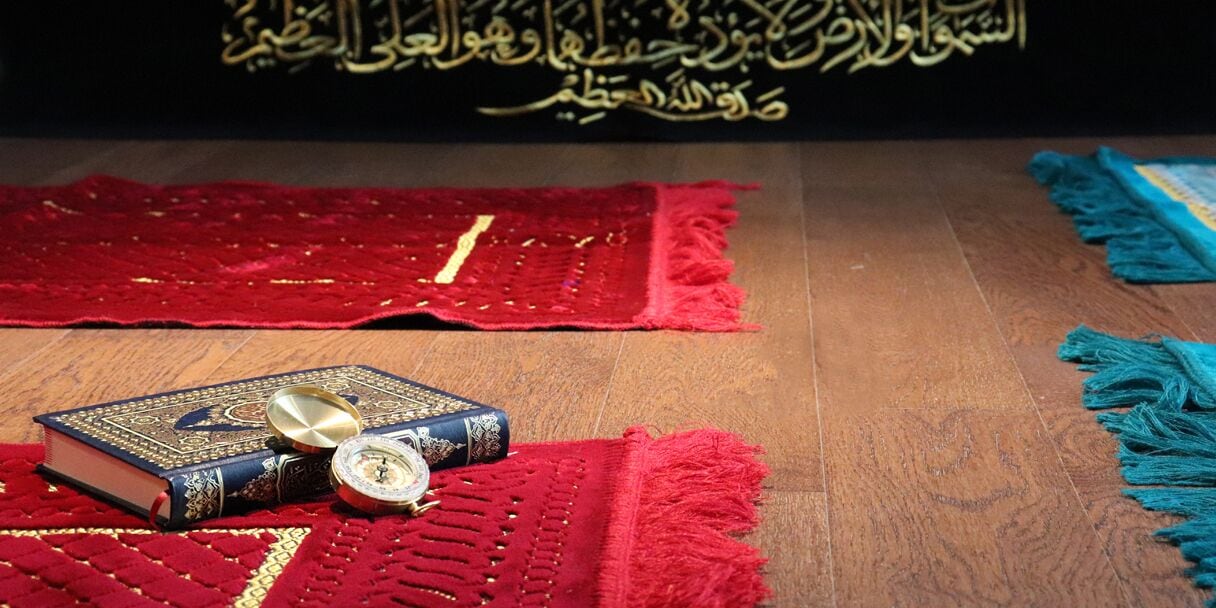 A wooden floor with a red and blue rug, a book, and a compass.
