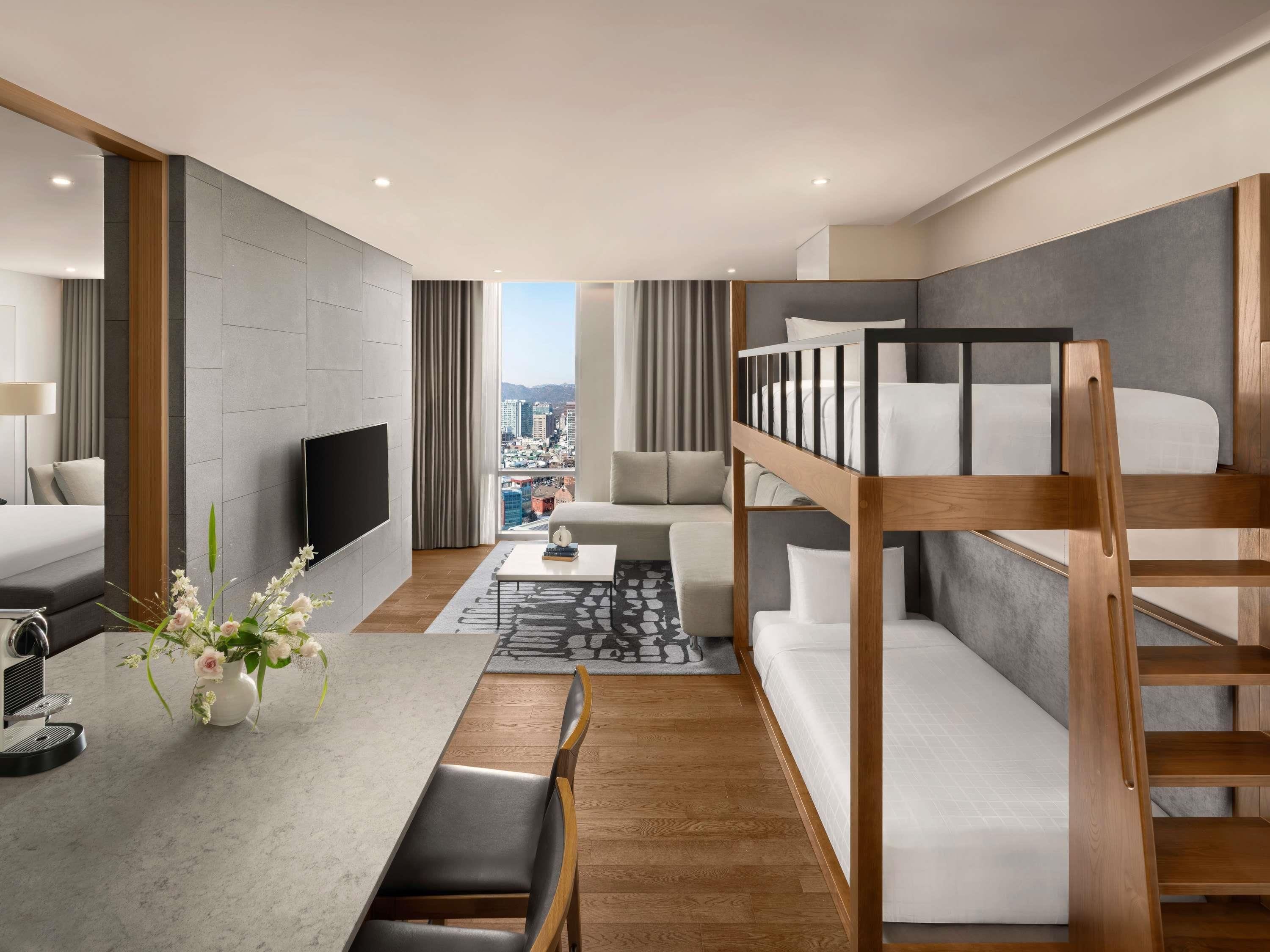 Une chambre d’hôtel moderne équipée d’un lit superposé, d’un téléviseur à écran plat, d’un coin repas avec une machine à café et offrant une vue sur la ville.