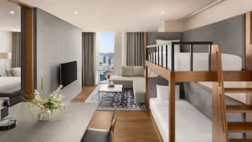 Une chambre d’hôtel moderne équipée d’un lit superposé, d’un téléviseur à écran plat, d’un coin repas avec une machine à café et offrant une vue sur la ville.