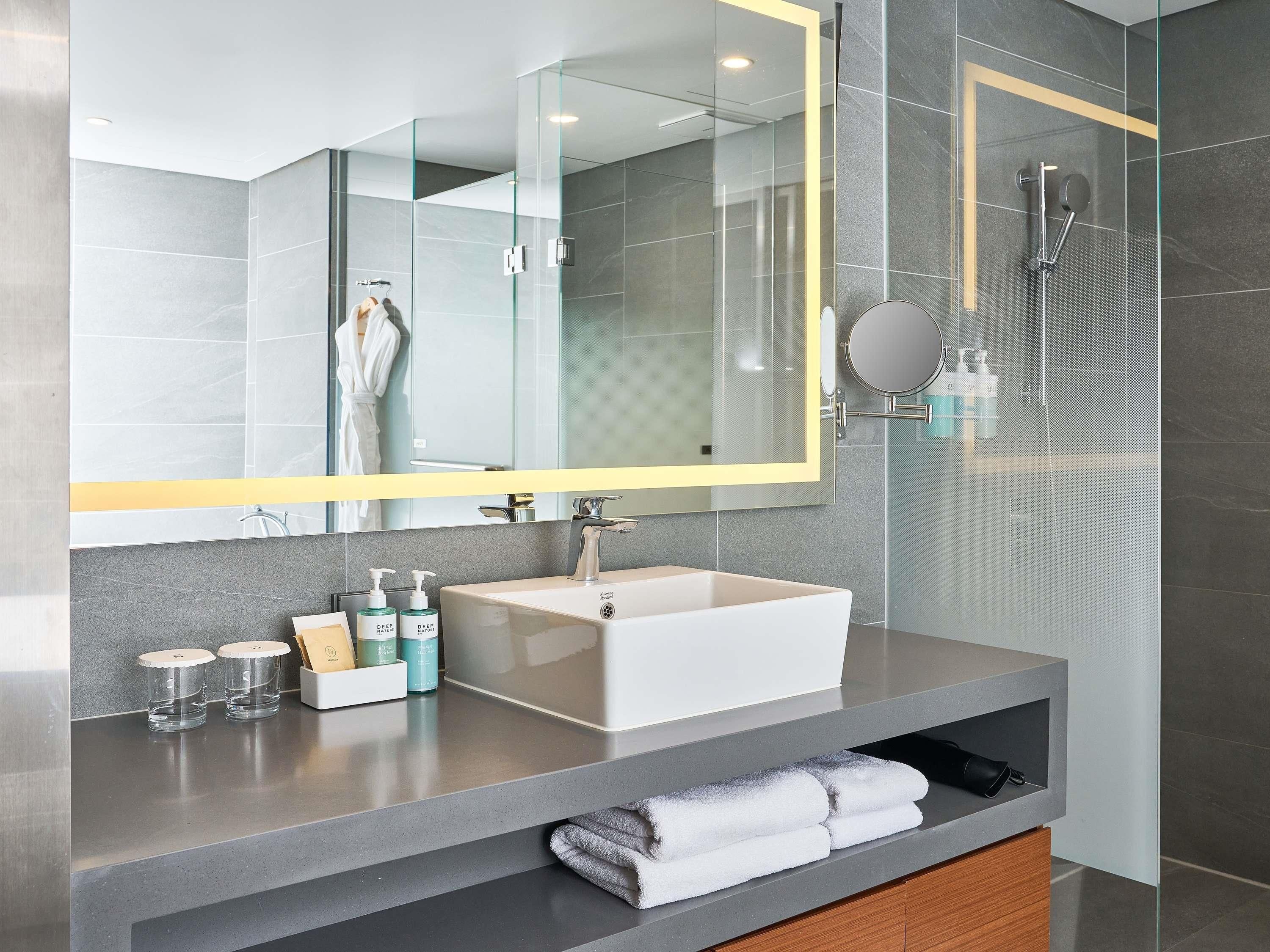 A modern bathroom with a large mirror, a white sink, and a glass shower enclosure.