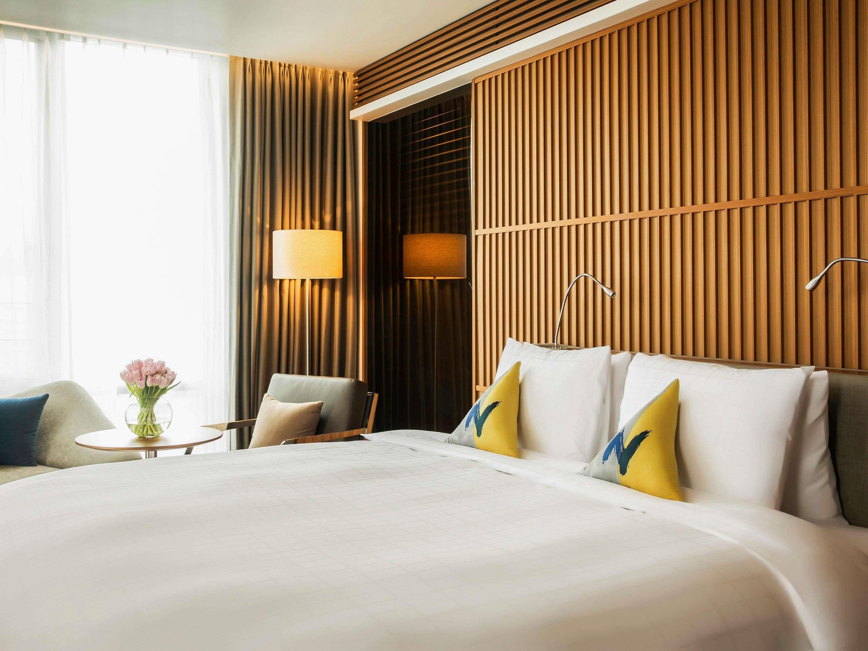 A hotel room with a large bed, a chair, a small table, and a lamp.