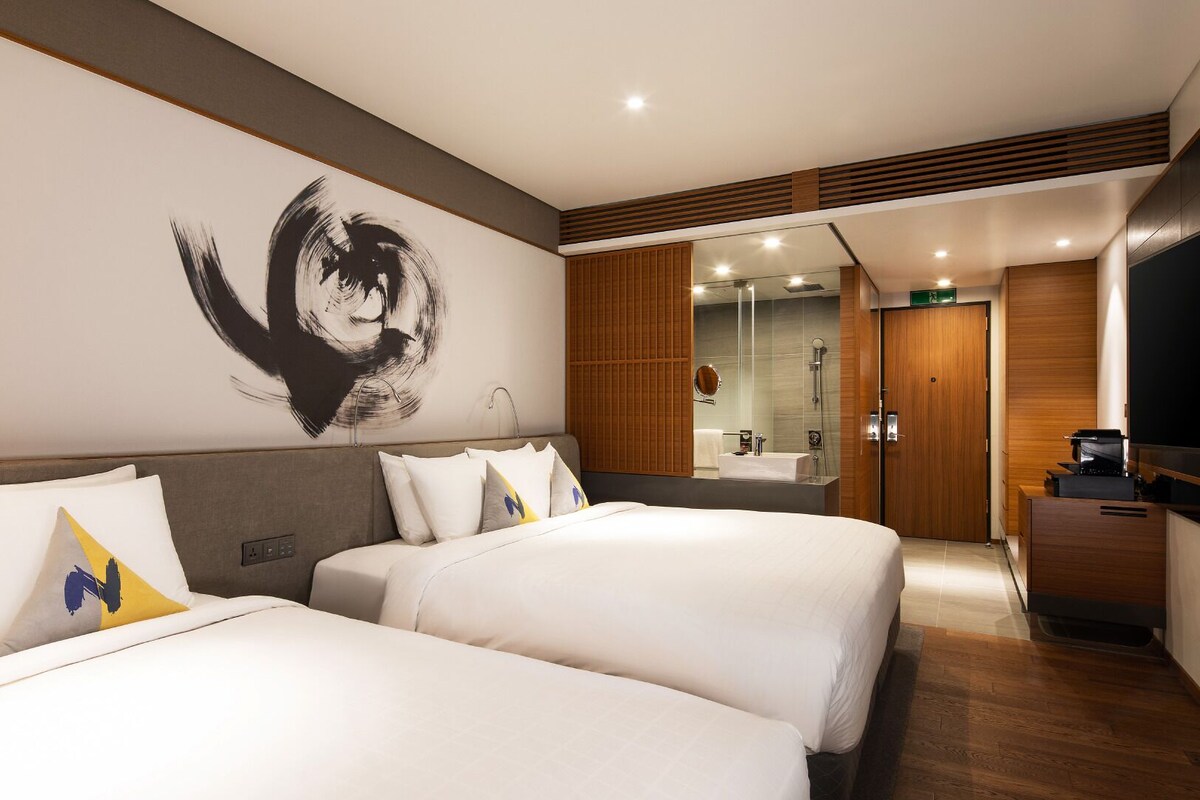 A hotel room with two beds, a large mirror, a TV, and a wooden panel wall.