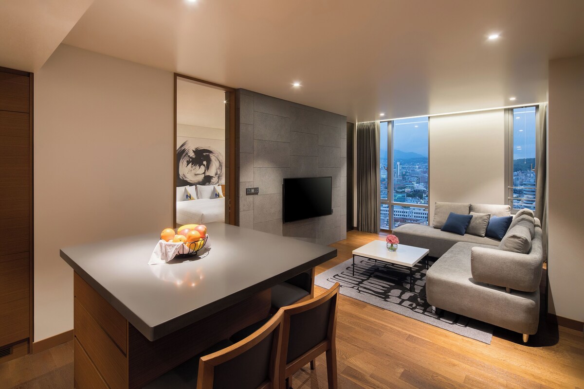 A modern living room with a sofa, a flat-screen TV, and a city view.